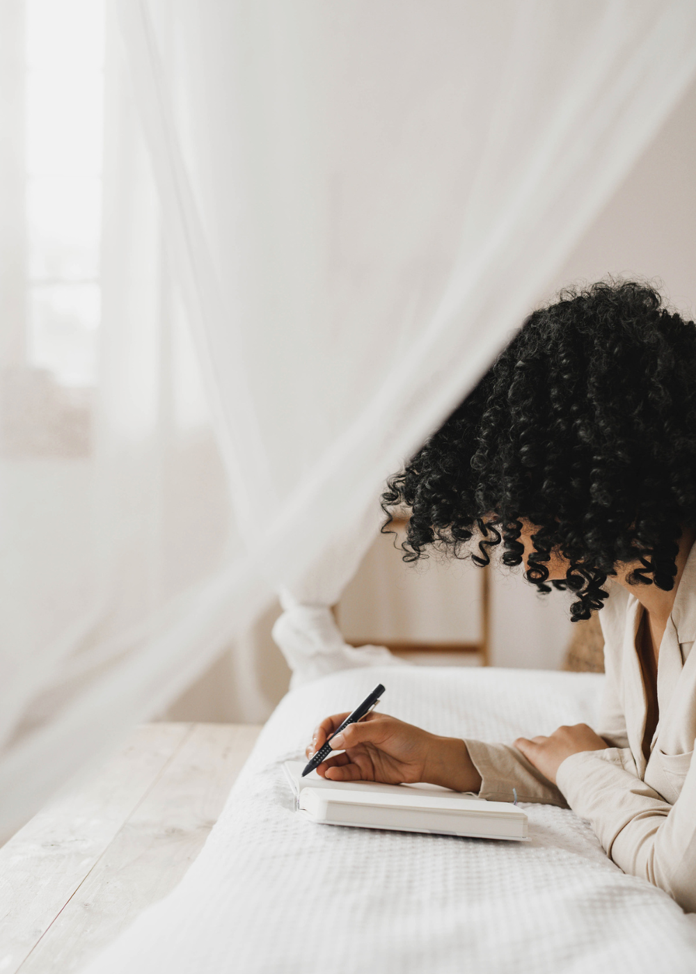 african american woman writing in her journal on her bed